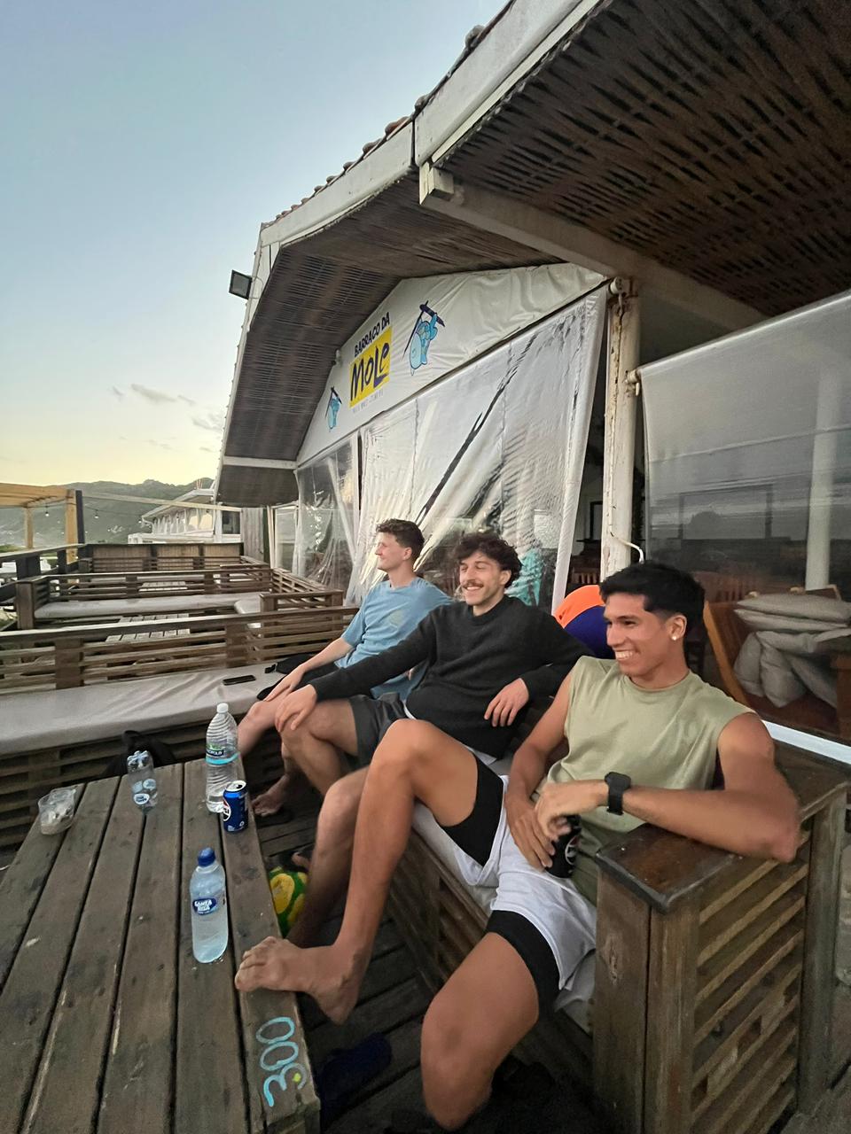 Gabriel rindo com amigos em um quiosque na praia